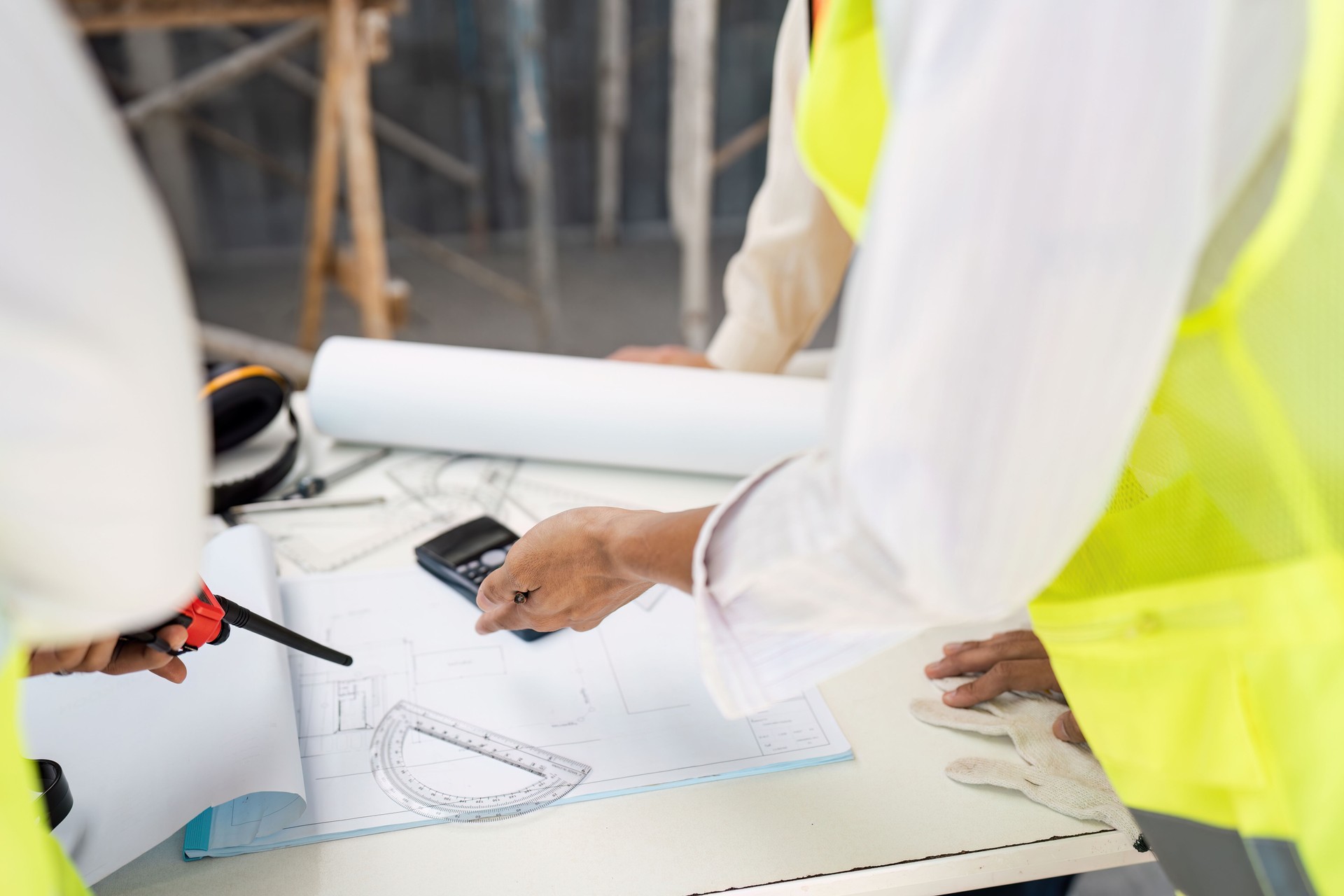 Architects Discussing Blueprints and Plans at a Construction Site with Safety Gear and Tools